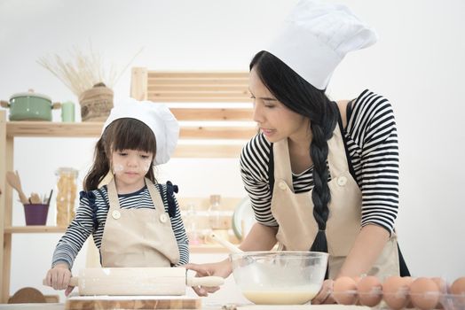 Asian mother and her daughter are preparing the dough to make a cake in the kitchen room on vacation.Photo series of Happy family concept.