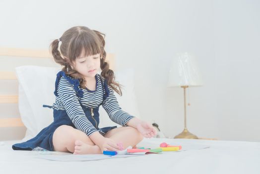 Cute asian little girl enjoy playing with toy set while sitting on bed in kid's bedroom at home.