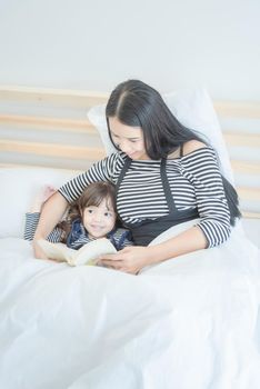 Happy loving family young asian mother reading funny book with her cute daughter in  bedroom.Photo design for family, children and happy people concept