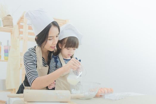 Happy family in the kitchen. Asian mother and her daughter preparing the dough to make a cake.Photo design for family, kids and happy people concept.