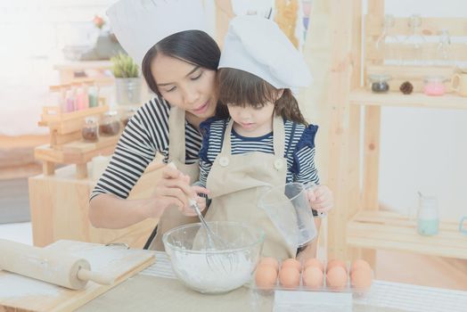 Happy family in the kitchen. Asian mother and her daughter preparing the dough to make a cake.Photo design for family, kids and happy people concept.