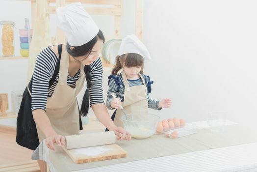 Happy family in the kitchen. Asian mother and her daughter preparing the dough to make a cake.Photo design for family, kids and happy people concept.