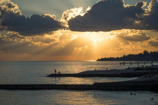 Coastline with beaches, breakwaters and people silhouette against a bright sunset and dramatic sky.