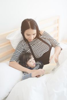 Happy loving family young asian mother reading a bed time story book to her daughter in  bedroom.Photo design for family, children and happy people concept