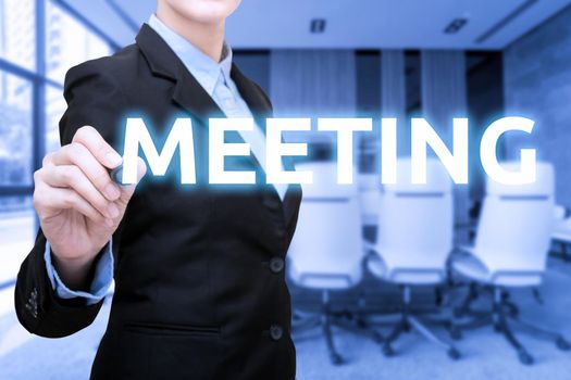 Business women writing Meeting word with blur meeting room and conference room in background.Photo for business corporation and teamwork concept