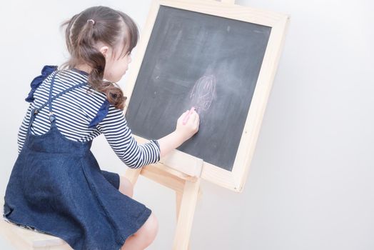 Happy asian girl kid draw cartoon with chalk on blackboard for learning at home. Photo for kid education and school study concept.