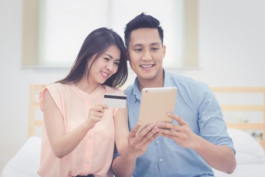 Happy Family,Asian couple lovers enjoy using smart tablet for online shopping together in bedroom.Photo series of family and happy people concept.