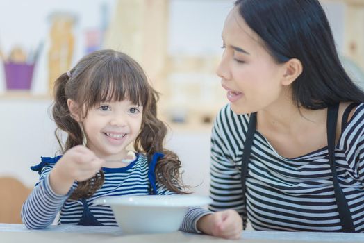 Happy family of asian mom feeding healthy breakfast to her cute daughter in the morning. Photo series of family, kids and happy people concept.