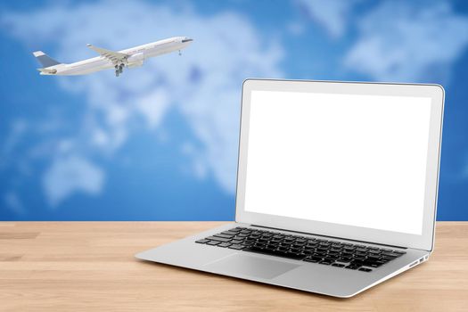 Smart laptop with white screen on wooden table with Commercial airplane flying over world map in background. Elegant Design with copy space for technology and travel concept.