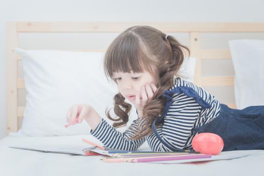 Cute little girl doing homework,writing and drawing with colourful pencils on bed at home. Elegant design for kid playing, preschool learn to write,read and creative art education concept