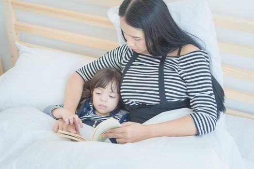 Happy loving family, Pretty young mother reading a bed time story book to her daughter in  bedroom.Photo design for family, children and happy people concept