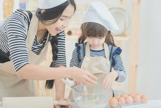 Happy loving family mother and her daughter cooking together to make a cake in kitchen room.Photo design for family, kids and happy people concept