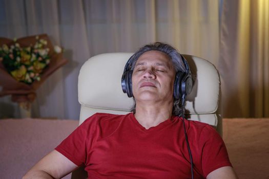 50-year-old man listens to music on headphones at home, sitting in a chair. Relaxing delight.