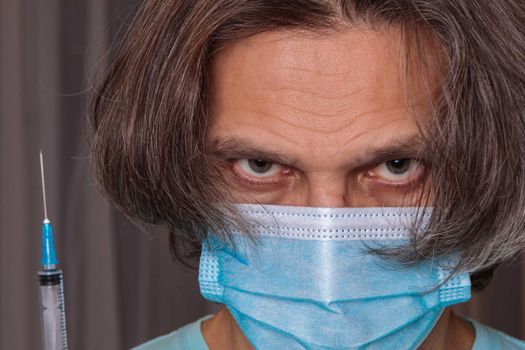 Adult man in a medical mask. Close-up eyes. Syringe in hand. Health safety concept