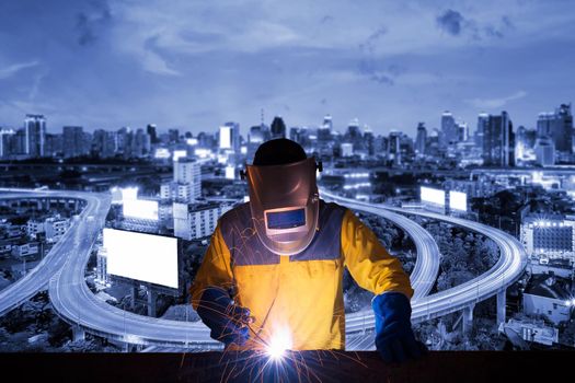 Welding worker welding steel structure with expressway and modern city in background for construction industrial work concept