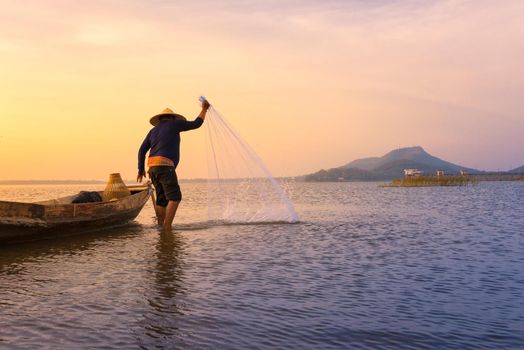 Asian fisherman with wooden boat throwing a net for catching freshwater fish in nature river in the early during sunrise time