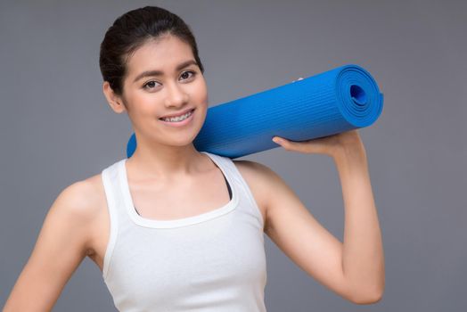 Young asian woman with happy smile holding her yoga mat at yoga healthy sport gym. Yoga and meditation have good benefits for health. Photo concept for Yoga Sport and Healthy lifestyle.