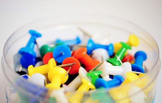 Heap of colorful office push pins on white background.