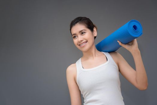 Young asian woman with happy smile holding her yoga mat at yoga healthy sport gym. Yoga and meditation have good benefits for health. Photo concept for Yoga Sport and Healthy lifestyle.