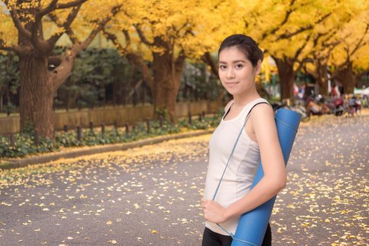 Young asian woman holding her yoga mat at outdoor park. Yoga and meditation have good benefits for health. Photo concept for Yoga Sport and Healthy lifestyle
