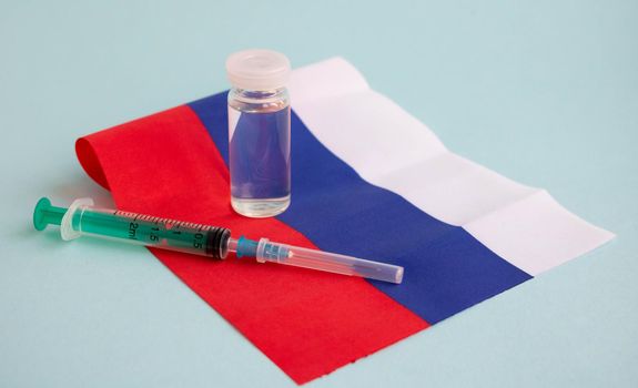 The vaccine and the injection syringe are on the small flag of Russia. For the prevention, immunization and treatment of coronavirus infection. The concept of medicine and healthcare.