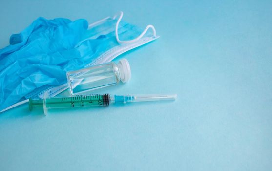 A syringe, gloves, mask, and a bottle of vaccine stand on a blue background. For the prevention, immunization and treatment of coronavirus infection. The concept of medicine and health care.