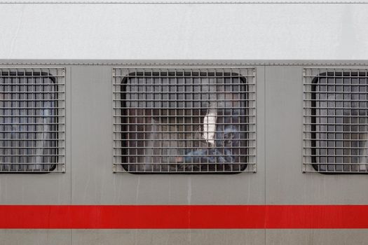 russian national guard officer inside of riot police truck window behind metal grate.