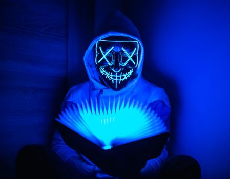 Man in glowing mask sitting in the corner with book-shaped lamp 