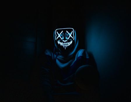 Man in glowing mask sitting in the corner