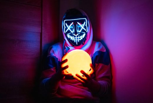 Man in glowing mask sitting in the corner with moon-shaped lamp 