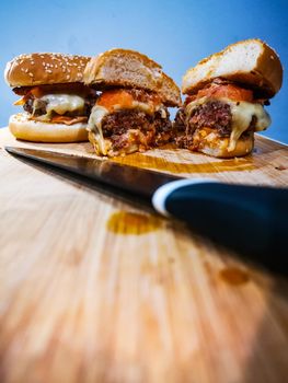 Black knife in front of burgers with beef cheese tomato and bacon