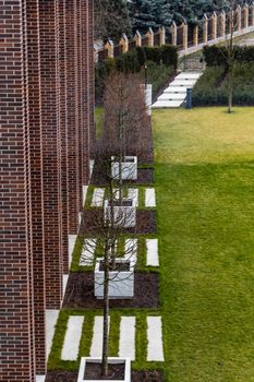 Small square with green glade with white tiles and trees near red brick building