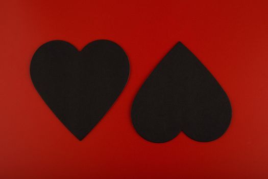 Top view of two black paper hearts against red background. Concept of love and St. Valentine's day