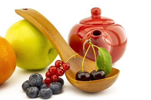 Fresh seasonal fruit still life with assorted berries including blueberries, cherries and red currants on wooden spoons with apple and orange and colorful red teapot