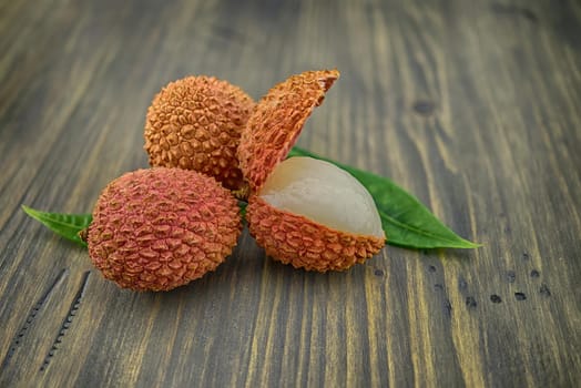 Lychee fruit whole and opened with green leaves decoration on rustic wood background