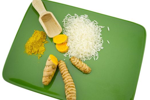 Fresh raw turmeric roots and slices next to heaps of rice and spice powder on a green plate with free space for text