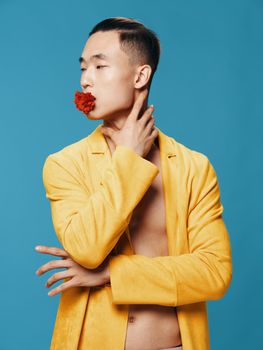 A guy in a yellow jacket on a blue background touches his head with his hand and a flower in his mouth. High quality photo