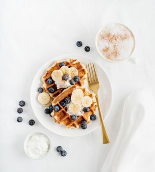 Top view of fresh made waffles with blueberries, banana and yoghurt, flat lay