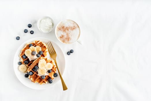 Top view of fresh made waffles with blueberries, banana and yoghurt, flat lay with copy space
