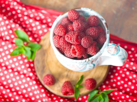 Ripe sweet raspberries in bowl on wooden table.