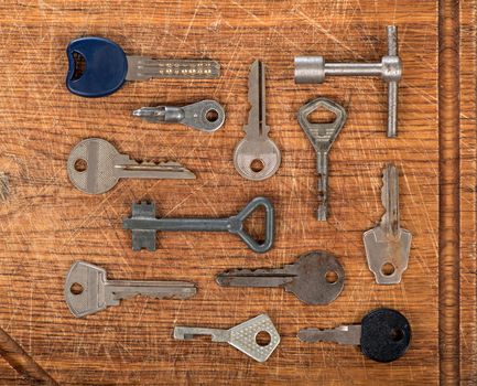 Many assorted old multi-colored metal antique vintage keys of different shapes on wooden scratched table background. Home security concept.