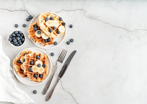 Top view of fresh made waffles with blueberries, banana and yoghurt, flat lay with copy space