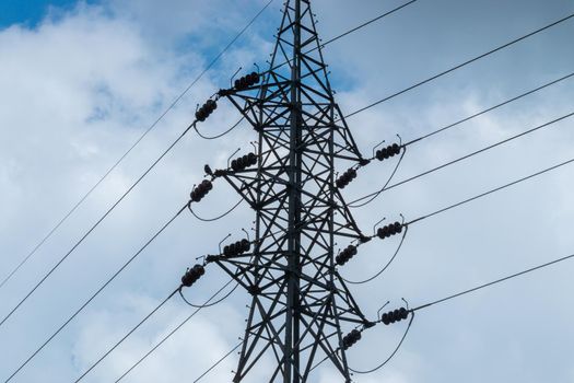 High voltage electric pylon and power lines against dark bloomy grey clouds.