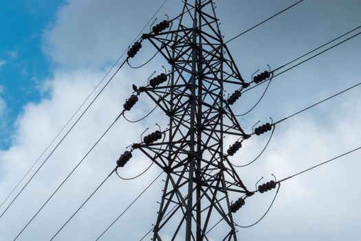 High voltage Electric tower pole silhouette and power lines against dark bloomy grey clouds.