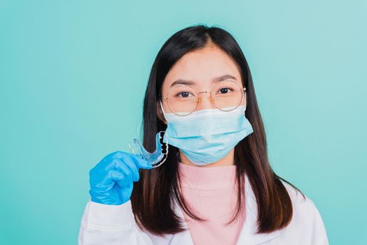 Asian beautiful woman dentist holding silicone orthodontic retainers for teeth on hand isolated blue background, Teeth retaining tools after removable braces, Orthodontics dental healthy care concept