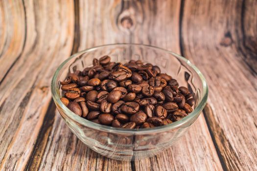 Freshly roasted coffee beans lie in a transparent glass vase on a wooden table