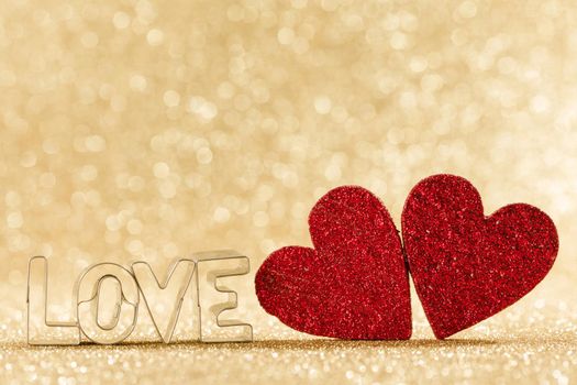 Two red handmade wooden hearts and word love on golden bright glitter lights bokeh background