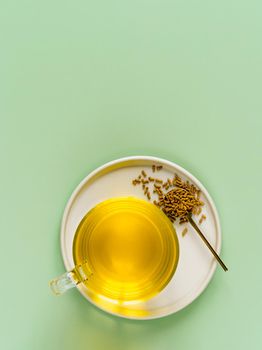cup of buckwheat tea on light green background. Top view of healthy soba tea and groats in spoon on green paper background. Flat lay. Copy space. Vertical