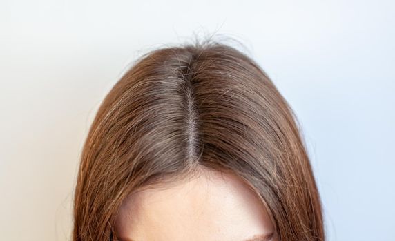 A woman's head with a parting of gray hair that has grown roots due to quarantine. Brown hair on a woman's head close-up.