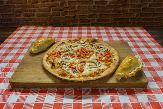 Traditional baked Argentine and Uruguay empanadas savoury pastries with meat beef stuffing against wooden background and pizza whit onion and red peppers.